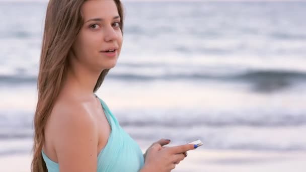 Young woman stays at sea beach holding and lookin at smartphone — Stock Video