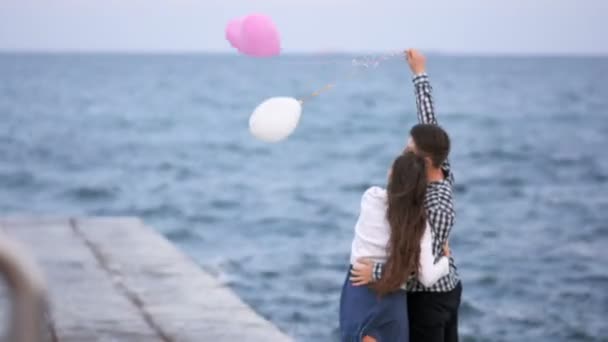 Pareja joven abrazos y globos vuelan lejos cerca del mar — Vídeo de stock