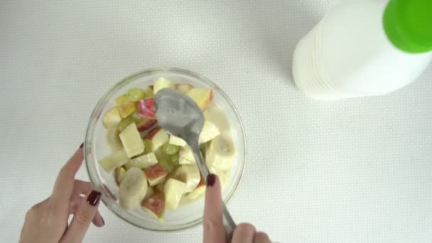 Belles mains de fille mélangeant salade de fruits dans un bol en verre — Video