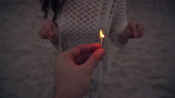 Mans hands helps woman to ignite sparklers at beach neat the sea in slow motion — Stock Video