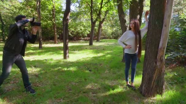 Fotografo che fotografa il modello tra gli alberi del parco . — Video Stock