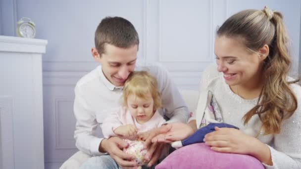 Young family with cute babygirl plays with money box — Stockvideo