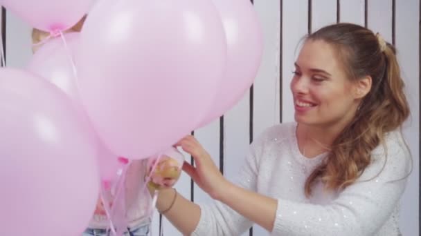 Een klein meisje speelt met roze en witte ballons en haar moeder in slow motion — Stockvideo