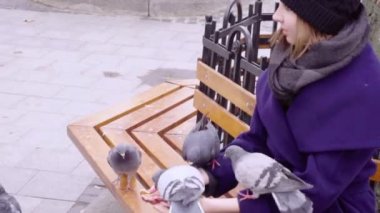 Bir kadın bir bankta oturur ve güvercinler beslemeleri