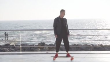 Deniz kenarında onun longboard üzerinde paten deri ceketli harika genç adam