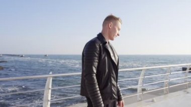 Genç adam onun longboard üzerinde deniz kenarında pateni deri ceket