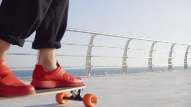 Kırmızı spor ayakkabılar erkekte longboard üzerinde deniz kenarında kaymaktadır.