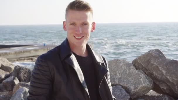 Jonge man in leren jas draagt zijn longboard en glimlacht — Stockvideo