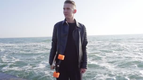 Jonge man houdt zijn longboard draagkracht door de zee — Stockvideo