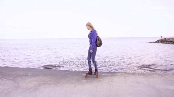 Joven hermosa chica monta su tabla de skate cerca del mar — Vídeos de Stock