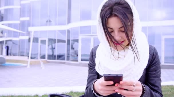 Mujer morena joven se sienta fuera con su teléfono — Vídeos de Stock