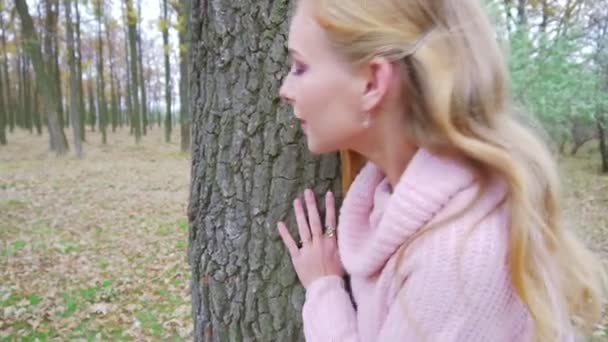 Attraente ragazza bionda nascosta nella foresta e appoggiata al vecchio albero, giocando — Video Stock