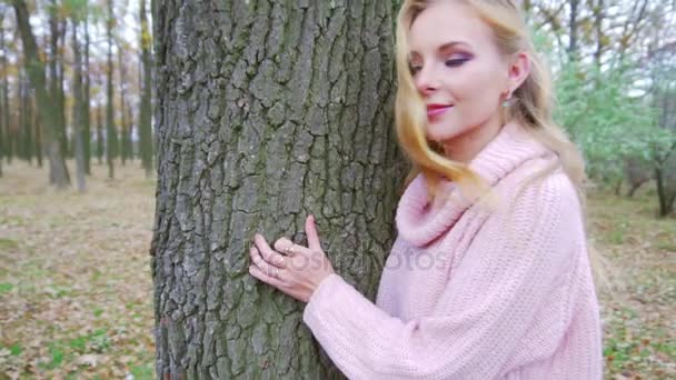 Привлекательная блондинка прячется в лесу и прислоняется к старому дереву, играя — стоковое видео