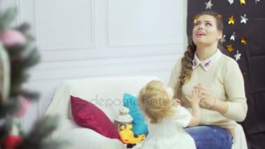 Tatlı bebeği Noel ağacı yakınındaki bir şekilde dekore edilmiş bir odada oynamaktan mutlu genç anne
