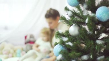 Tatlı bebeği Noel ağacı yakınındaki bir şekilde dekore edilmiş bir odada oynamaktan mutlu genç anne