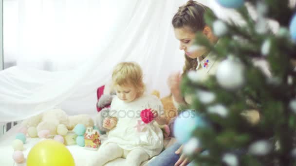 Feliz joven madre jugando con su dulce bebé en una habitación decorada cerca del árbol de Navidad — Vídeo de stock