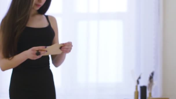 Jovem mulher bonita em vestido preto abre um envelope e lê uma carta — Vídeo de Stock
