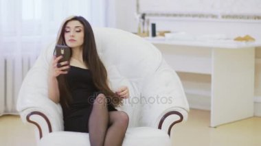 Studio akıllı telefonunu kullanarak vintage beyaz koltuk üzerinde poz güzel genç model kadın