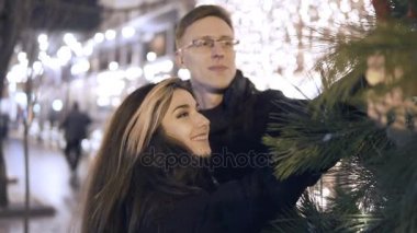 Geceleri mutlu çekici çift ayakta yakınındaki bir Noel pazarda yeni yıl ağacı. Güzel ışıklar arka plan.
