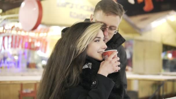 Glückliches attraktives Paar, das nachts auf einem Weihnachtsmarkt Tee trinkt. schöne Lichter Hintergrund. — Stockvideo