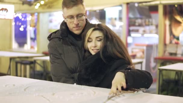 Young couple paints using their fingers on the snow. Beautiful lightening bachkground. Christmas time. — Stock Video