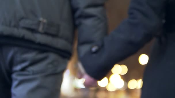 Pareja joven camina togerher cerca de las luces de Navidad en el mercado de Navidad. De la mano . — Vídeos de Stock