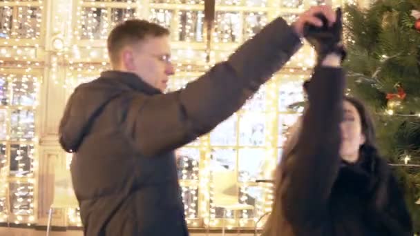 Ein glückliches, attraktives Paar tanzt nachts auf einem Weihnachtsmarkt neben dem Neujahrsbaum. schöne Lichter Hintergrund. — Stockvideo