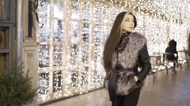 Unga vackra vackra kvinna går leende på city gatan i natt mot starkt ljus — Stockvideo