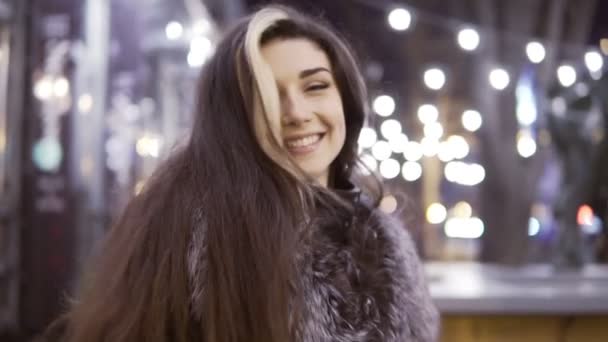 Joven hermosa mujer bonita sonriendo en la calle de la ciudad en la noche contra las luces de la noche — Vídeos de Stock