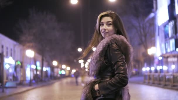 Jovem bela mulher bonita posando na rua da cidade na noite contra as luzes da noite — Vídeo de Stock