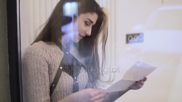 Retrato de mujer joven y elegante con pelos marrones leyendo carta y sonriendo. Luego lo pone sobre la mesa. — Vídeo de stock