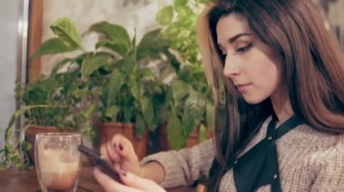 Koşum cep telefonuyla kafede genç esmer kadın alır bir mesaj ve gülümsüyor. Masada sıcak kakao fincan.