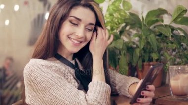 Koşum istimal hareket eden telefon ve sıcak kakao bir fincan içme kafede genç esmer kadın. Bir iletiyi aldıktan sonra gülümseyerek başlar.