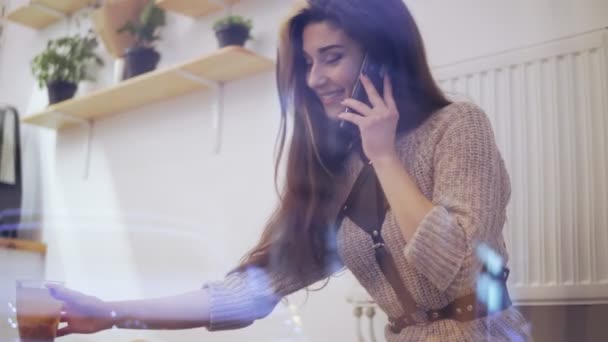 Jovem morena vista pela janela conversando ao telefone, sorrindo e bebendo chá — Vídeo de Stock