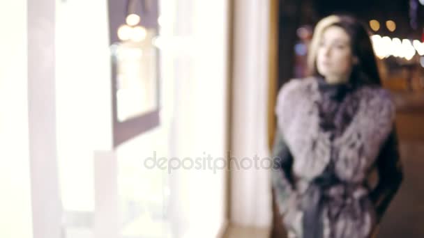 Winter dressed young woman comes up to the window display of expensive boutique store and stands in front of it. — Stock Video