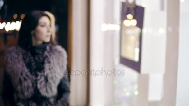 Mujer joven vestido de invierno se acerca a la pantalla de la ventana de la tienda boutique caro y se para delante de ella . — Vídeos de Stock
