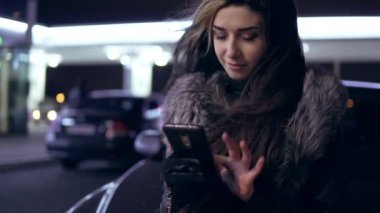 Genç güzel esmer kadın ceket araba kukuleta oturan onun smartphone kullanır