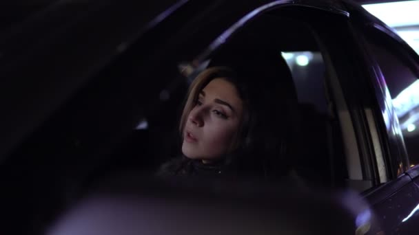 Молодая красивая брюнетка в пальто сидит в машине и пьет горячий напиток ночью зимой — стоковое видео