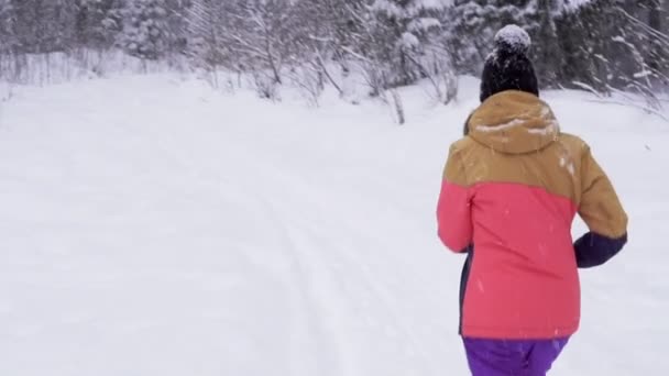 Νεαρή γυναίκα τρέχει στο χιόνι στην χειμωνιάτικα ρούχα — Αρχείο Βίντεο