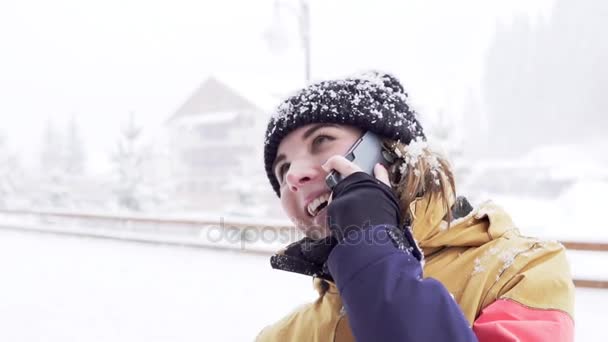 Портрет крупным планом девушки, разговаривающей по телефону и смеющейся на улице. Идёт снег. . — стоковое видео