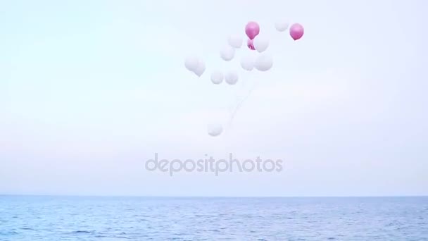 Roze en witte ballons vliegen in de lucht onder de zee. — Stockvideo