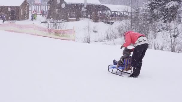 Bukovel, Ukraine på 28 December: kvinna får barnet redo att flytta på släde genom snödrivor — Stockvideo