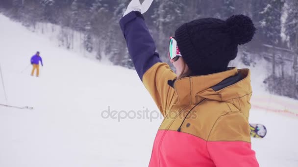 Young sporty woman in ski glasses smiling and waving with her hand calling someone — Stock Video