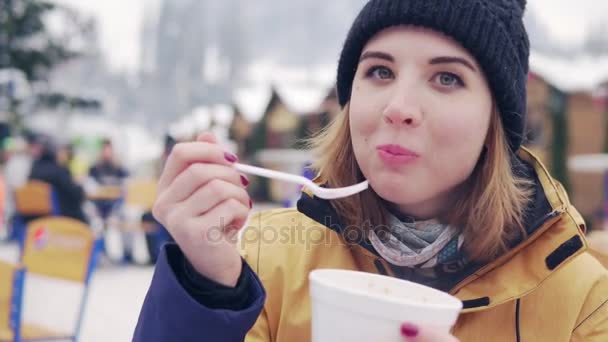 Schöne Blondine isst Pilav vor dem Hintergrund des Wintermarktes — Stockvideo