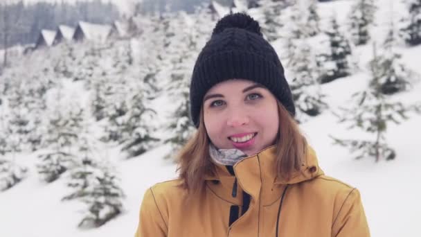 Jonge vrouw met heldere winter kleding tegoed buiten. Besneeuwde bos op de achtergrond. — Stockvideo