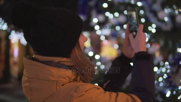 Jonge vrouw in lichte winterkleren, het nemen van foto met mobiele telefoon op de kerstmarkt — Stockvideo