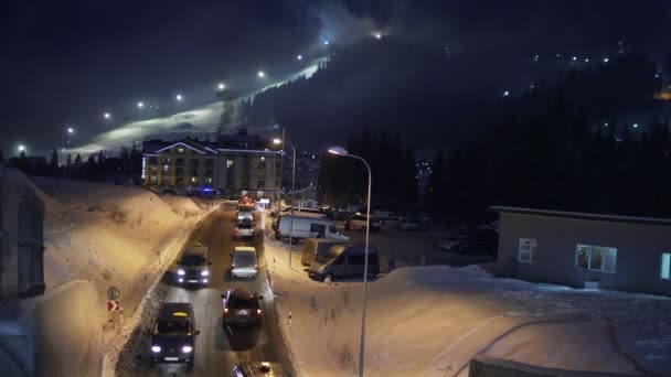 Bukovel, Ukraine - 26. Dezember: Verkehr auf der Straße vom Ferienort in der Nacht. Nachtskifahren und Snowboarden in einem Skigebiet im Hintergrund. Bukovel ist das größte Skigebiet der Ukraine. — Stockvideo