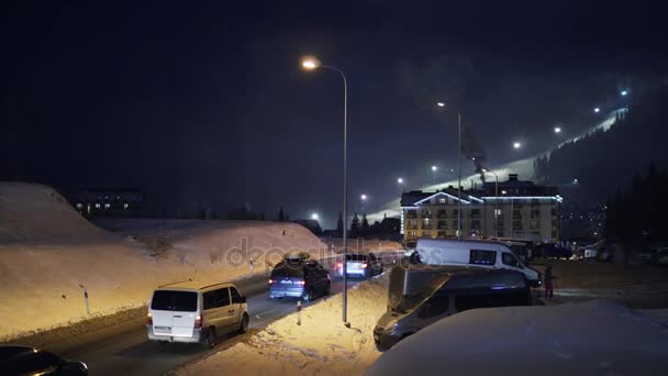 БУКОВЕЛ, УКРАИНА - 26 декабря: Движение по дороге от курорта ночью. Ночные лыжи и сноуборд на лыжном курорте на заднем плане. Буковель - крупнейший горнолыжный курорт Украины . — стоковое видео