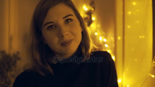 Portrait of a young woman with fairy lights in the house — Stock Video