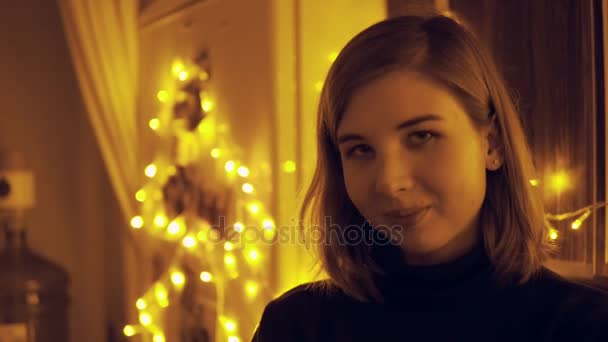 Porträtt av en ung kvinna med älva lampor i huset vifta med handen till någon nära — Stockvideo